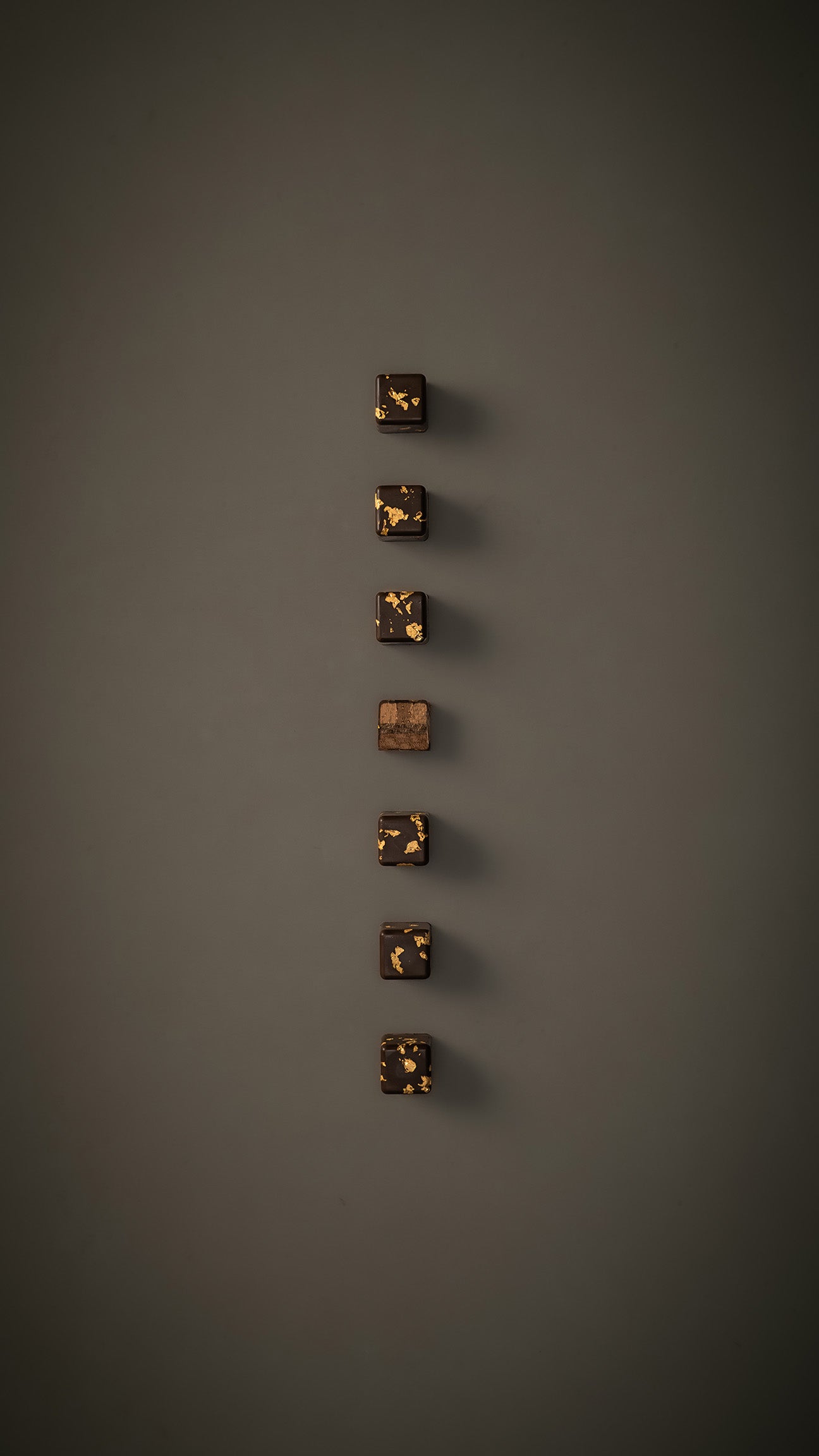 7 Kaffee Karamell Pralinen auf beige-grauem Hintergrund. Eine Praline in der Mitte durchgeschnitten.