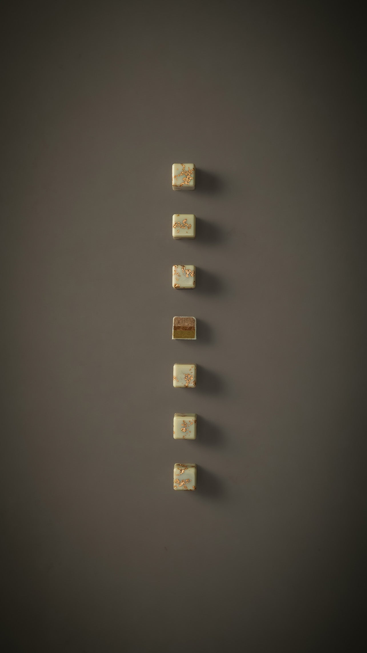 7 Zitrone-Pistazie Pralinen auf beige-grauem Hintergrund. Eine Praline in der Mitte durchgeschnitten.