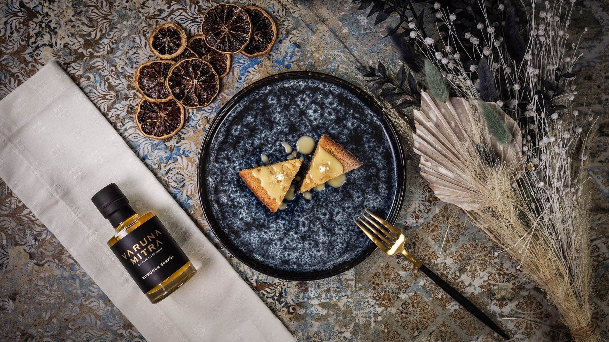 Moelleux au Citron, Zitronenschnitten, mit Zitronenzuckerguss und Fleur de Sel Zitrone neben einer Flasche Varuna Mitra Zitronenöl