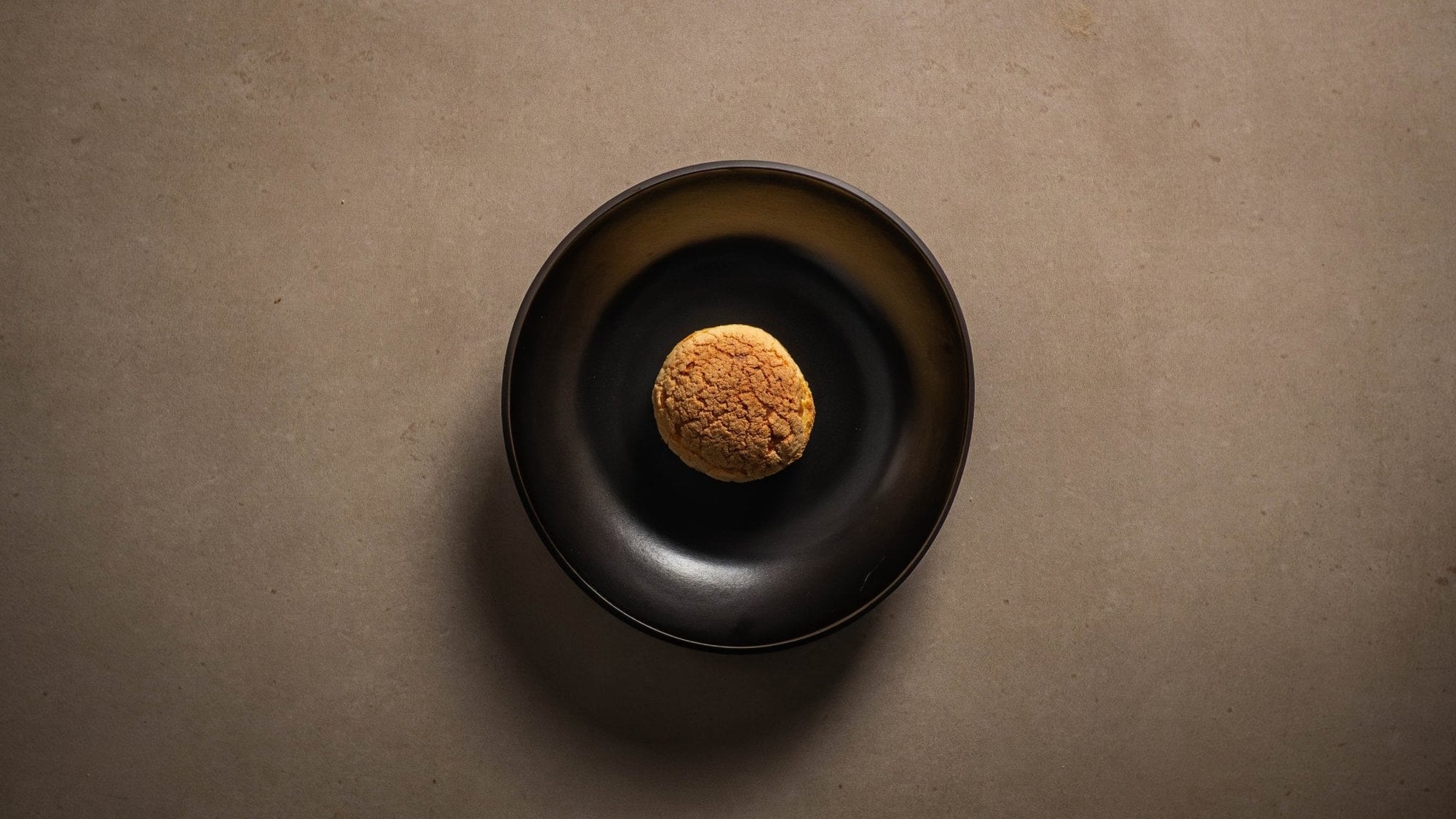 Choux au Craquelin mit cremiger Kaffee Mascarpone und Salted Caramel serviert auf einem schwarzen Teller.