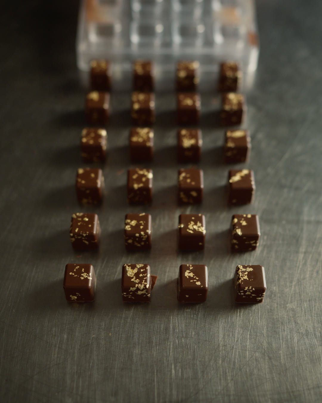 Varuna Mitra Kaffee-Karamell Praline mit Blattgold frisch aus der Form auf einem Edelstahltisch beim Pralinen herstellen