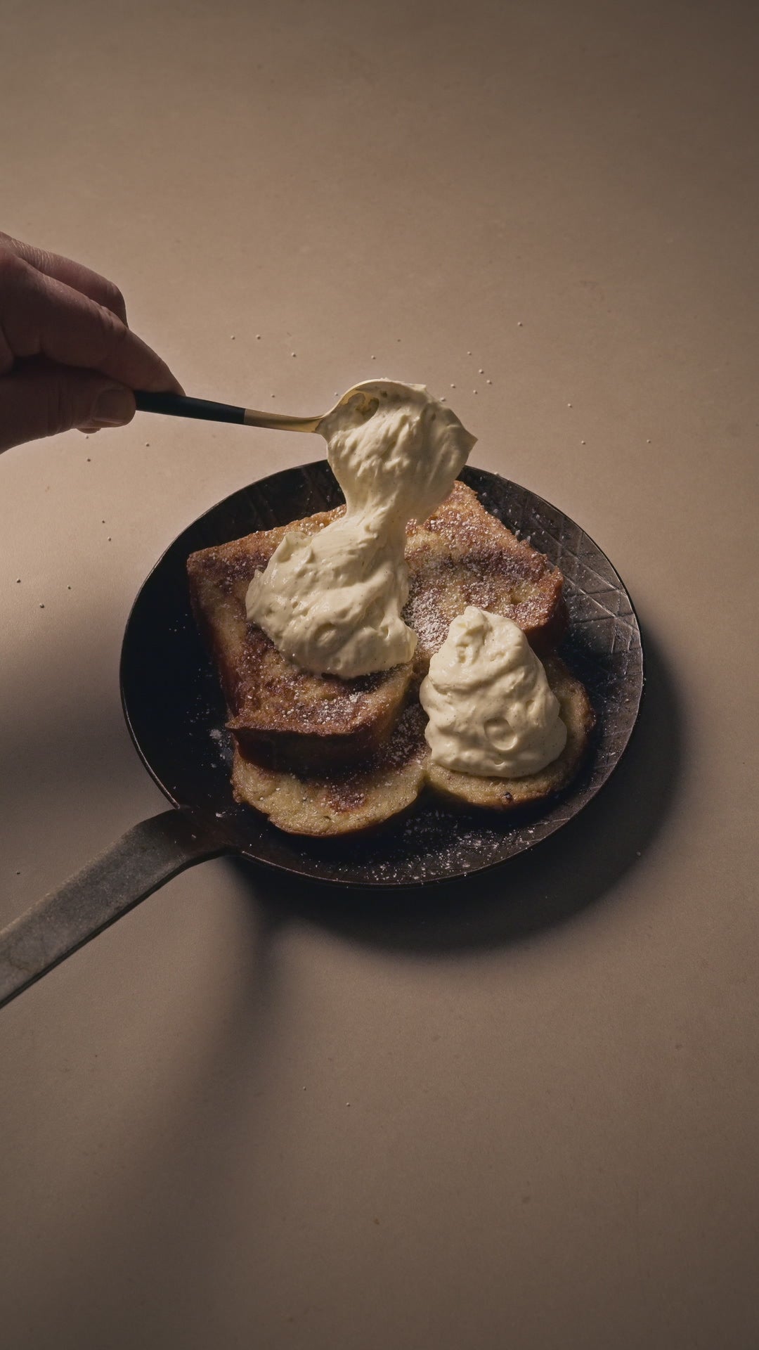 Rezept French Toast wird mit Kaffee Mascarpone in einem goldenen Löffel drapiert. French Toast in einer Eisenpfanne auf hellem Stein.