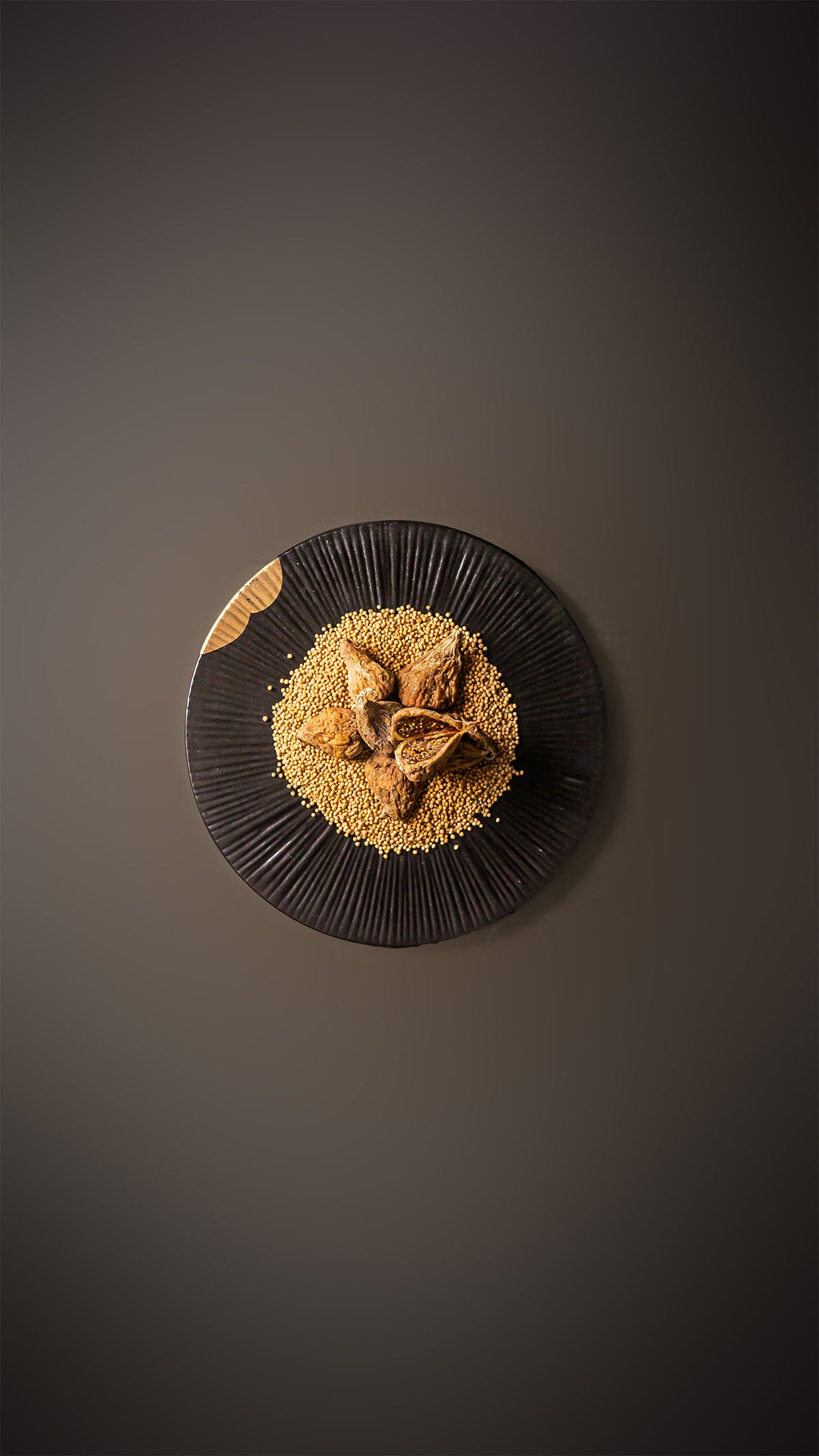 Spanische Goldfeigen auf gelber Senfsaat, auf schwarzem Teller, auf beige-grauem Hintergrund.