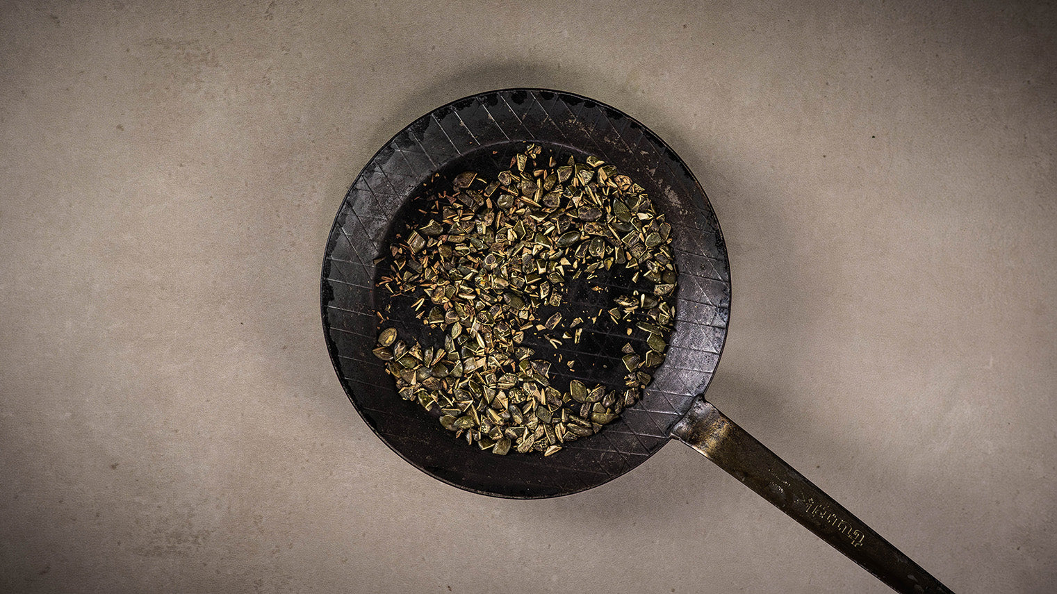Kürbiskerne in einer Gusspfanne rösten. Pfanne steht auf hellem Stein.