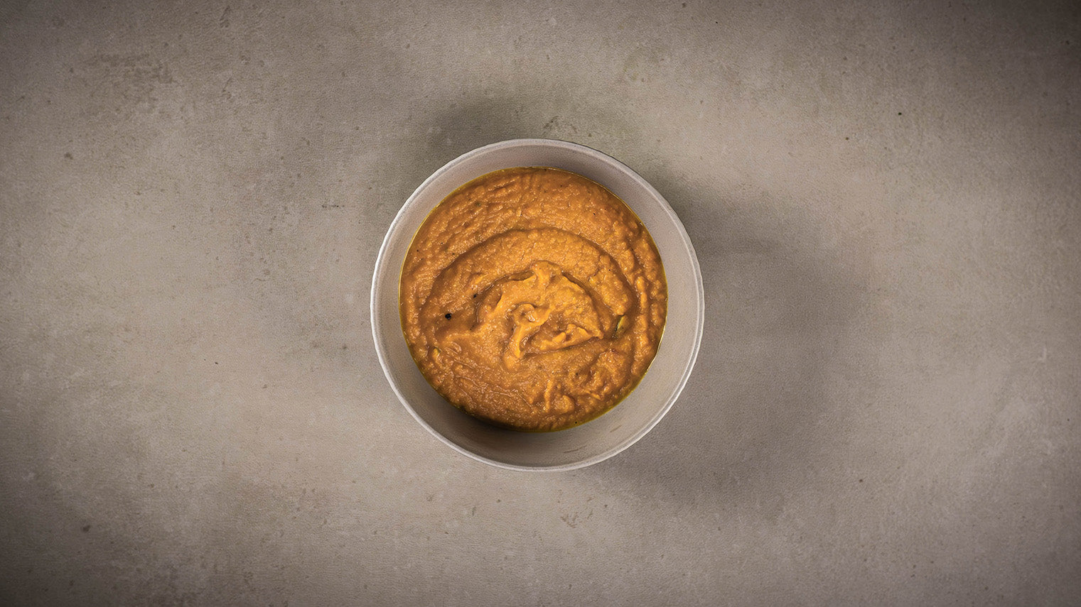 Kürbispüree in einer weißen Schale auf hellem Stein.