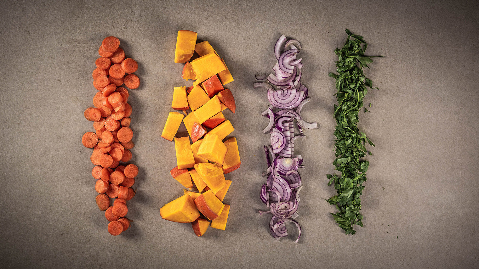 Kürbis, Karotten, Zwiebeln und Kräuter geschnitten auf hellem Stein.