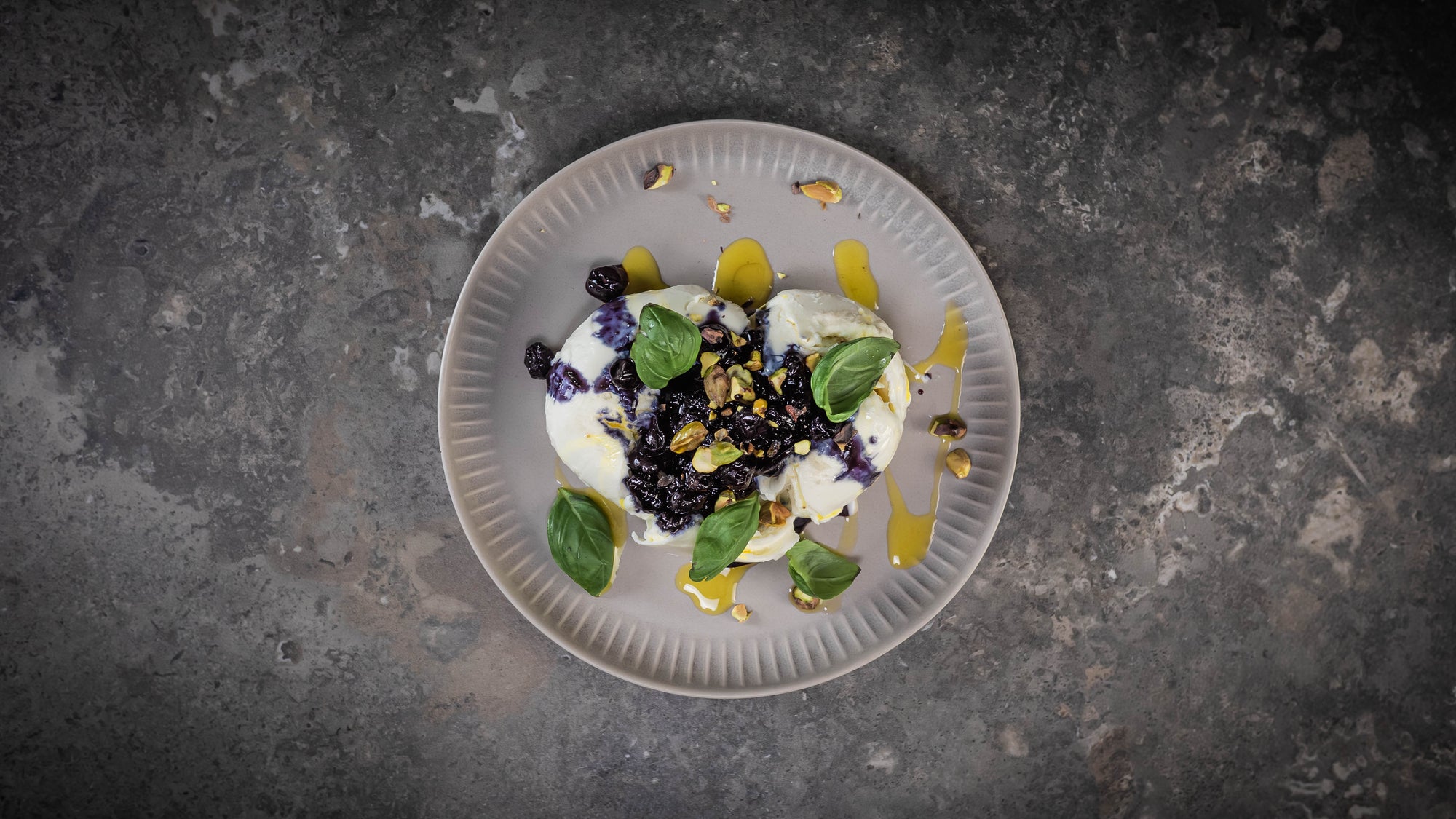 Mozzarella mit Blaueren und Zitronenöl auf einem beigen Teller dekoriert mit Basilikum und Pistazien.