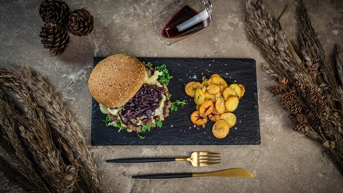 Rezept Wildburger mit Camembert, Chili Mayo und Bratkartoffeln auf einer Schieferplatte und dazu ein Glas Rotwein.