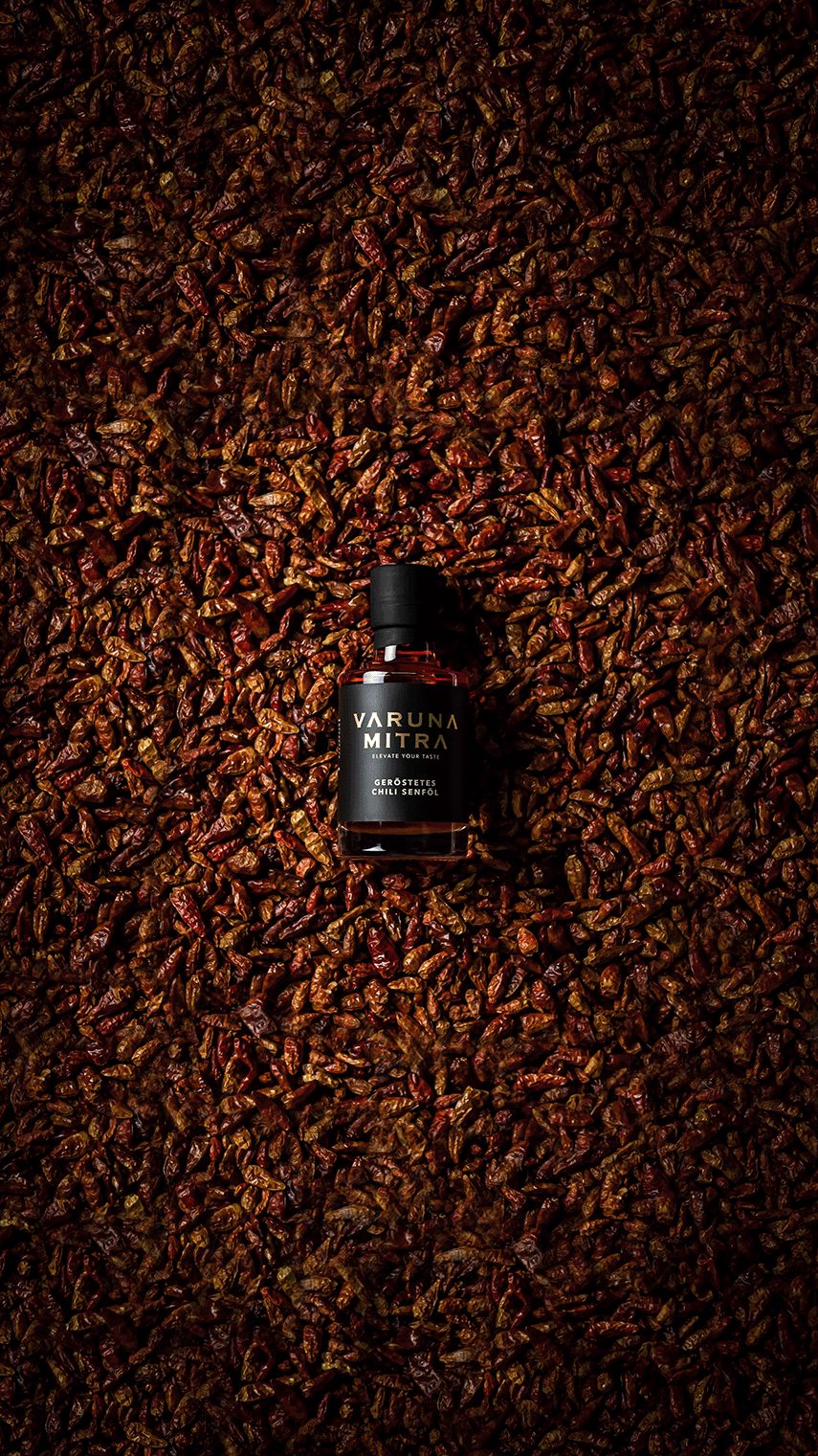Varuna Mitra Chili Öl Flasche auf einem Bett von Chilis.