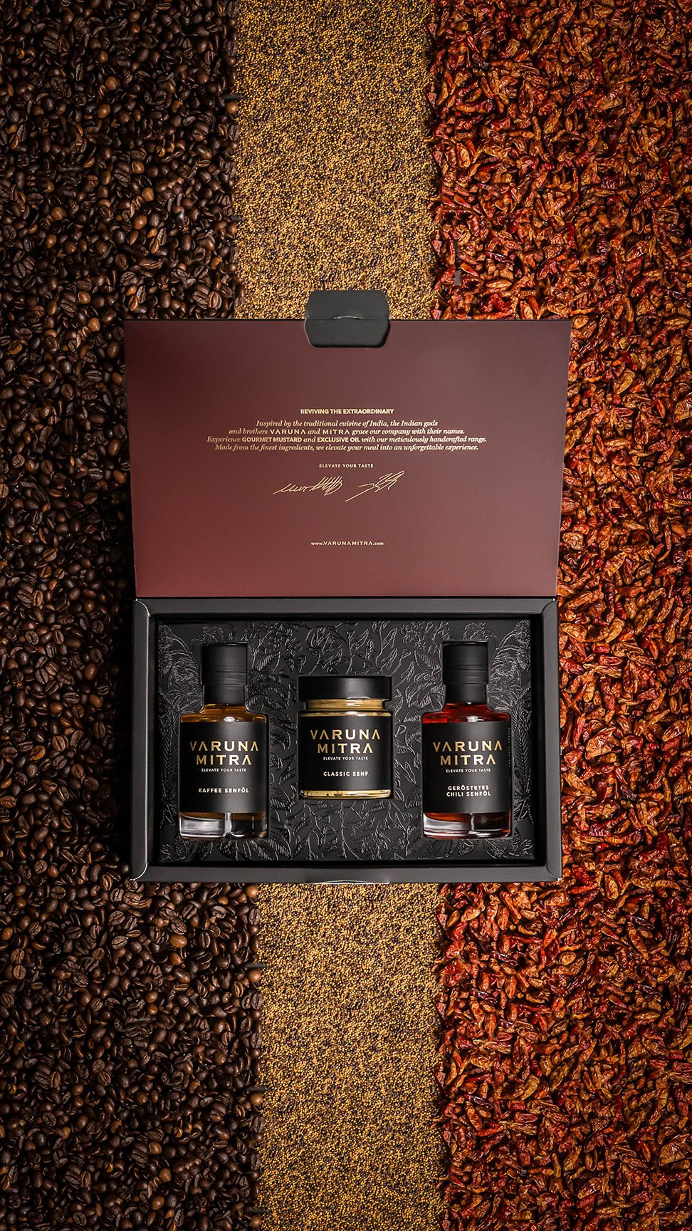 Varuna Mitra Geschenkbox Varuna mit zwei Flaschen Öl und einem Senf auf einem Bett aus Kaffeebohnen, Senfsaat und Chilis.