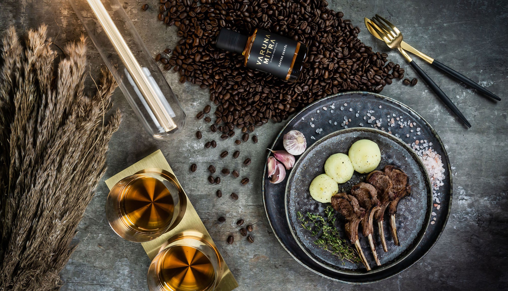 Varuna Mitra Kaffee Oel Flasche auf Kaffeebohnen mit Lammkarrees auf blauem Teller, garniert mit Kartoffelpüree, Rauchsalz und Knoblauch.
