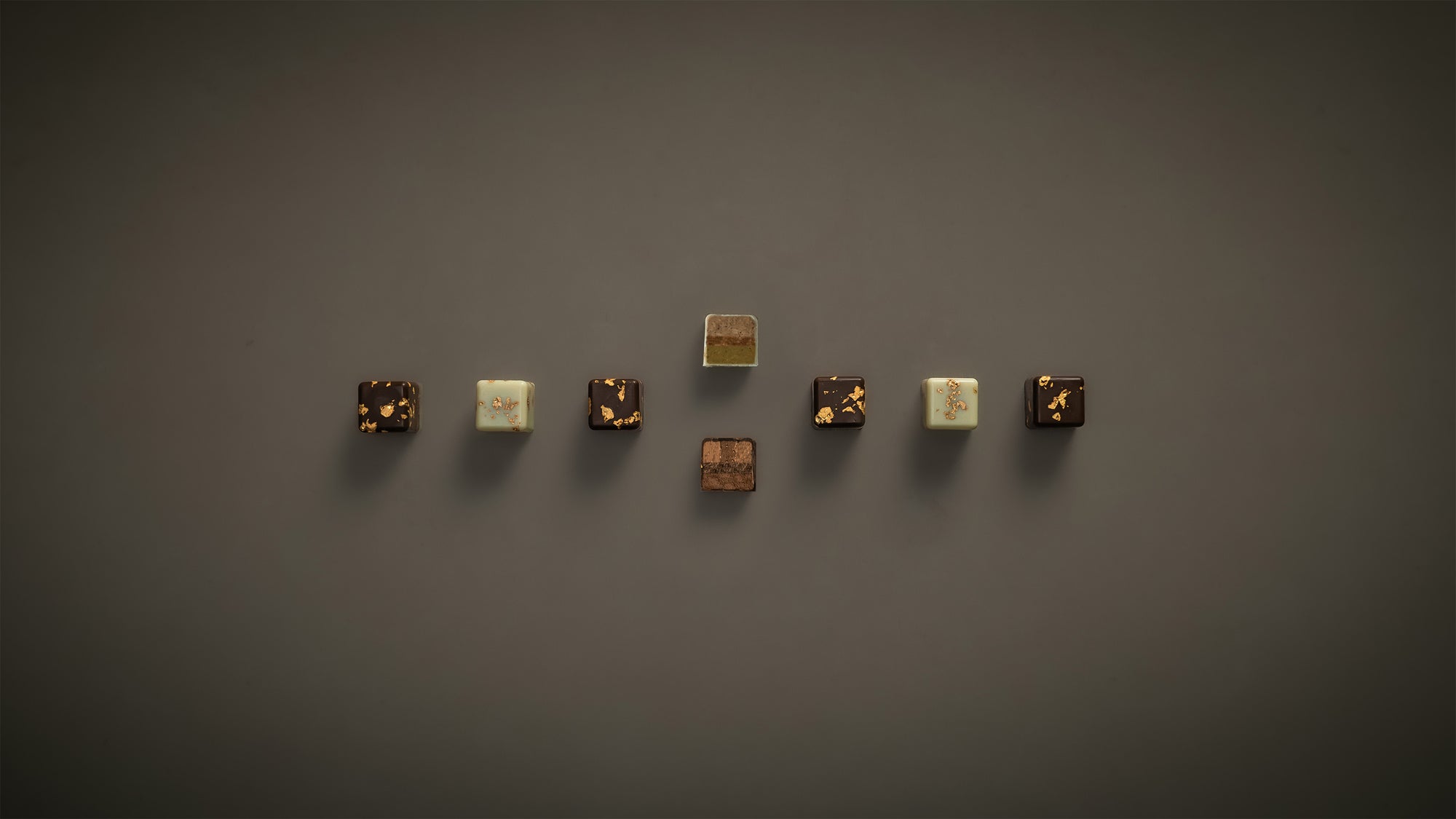 8 Kaffee-Karamell und Zitrone-Pistazie Pralinen auf beige-grauem Hintergrund. Zwei Praline in der Mitte durchgeschnitten. Horizontal angerichtet